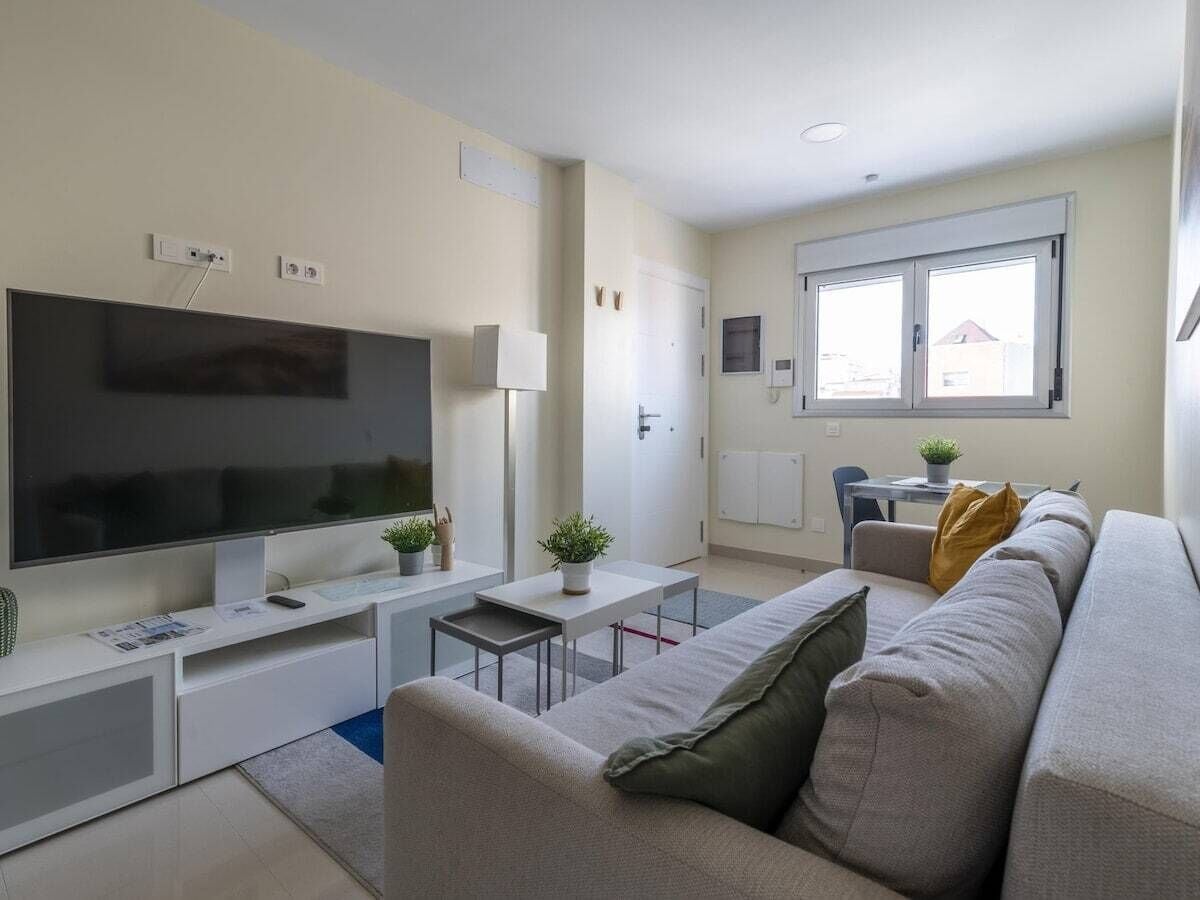 A modern living room with a flat-screen TV, a sofa, a coffee table, and a dining area with a table and chairs.