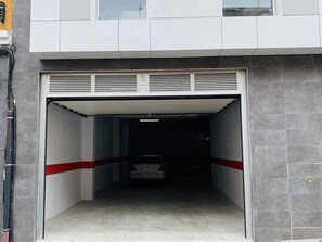 Entrada de um estacionamento com um carro dentro, paredes cinzentas e uma faixa vermelha no chão.
