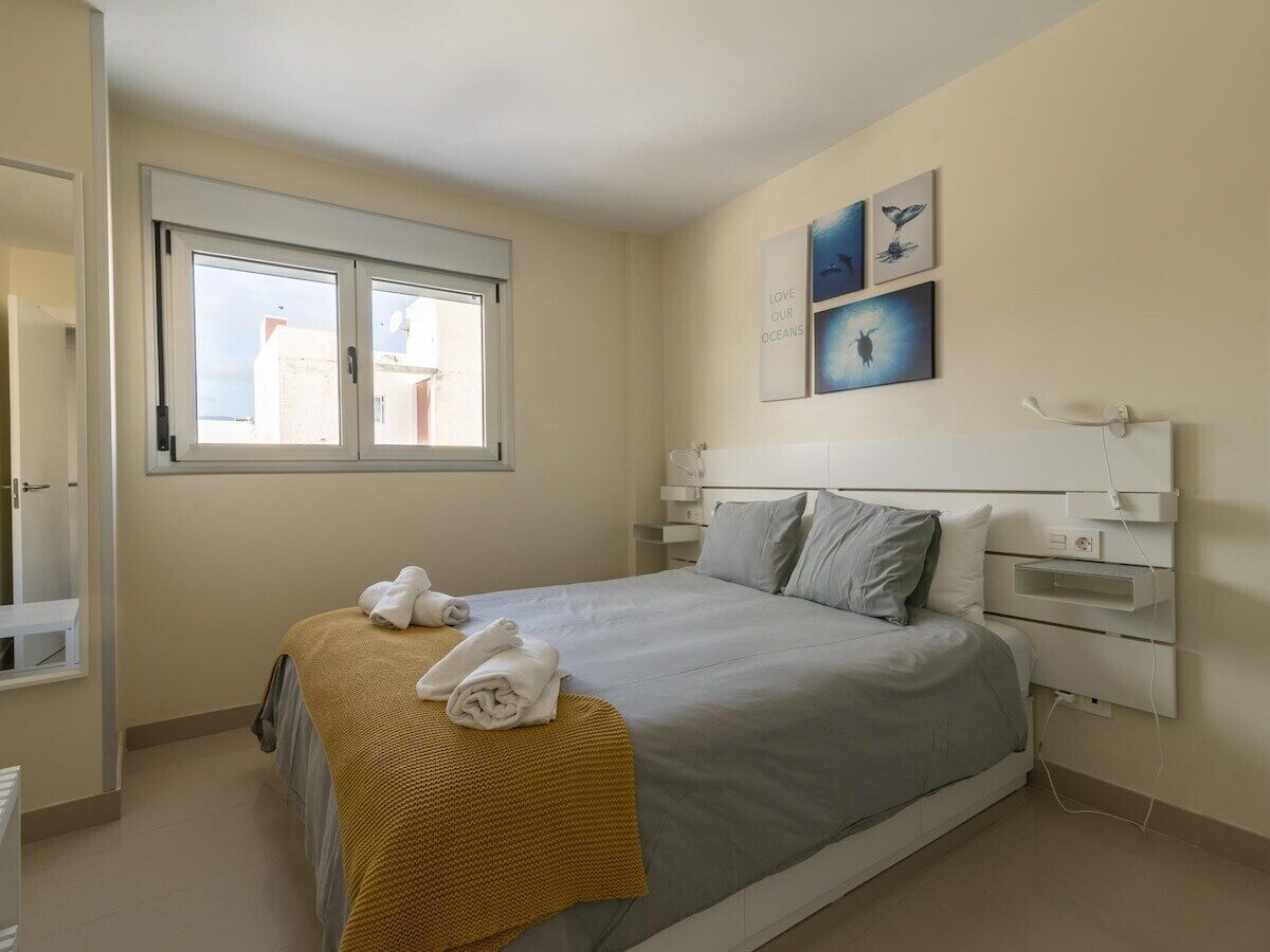A bedroom with a bed, a window, a bedside table, and wall art.