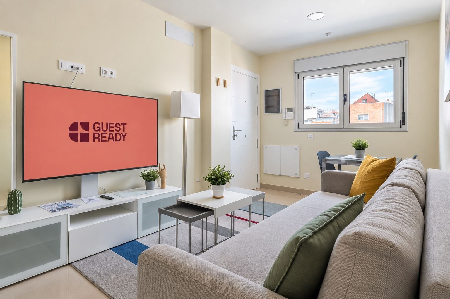 Un salon moderne doté d’un téléviseur à écran plat affichant le message « PRÊT POUR LES INVITÉS », d’un canapé, d’une table basse et d’un petit coin repas.