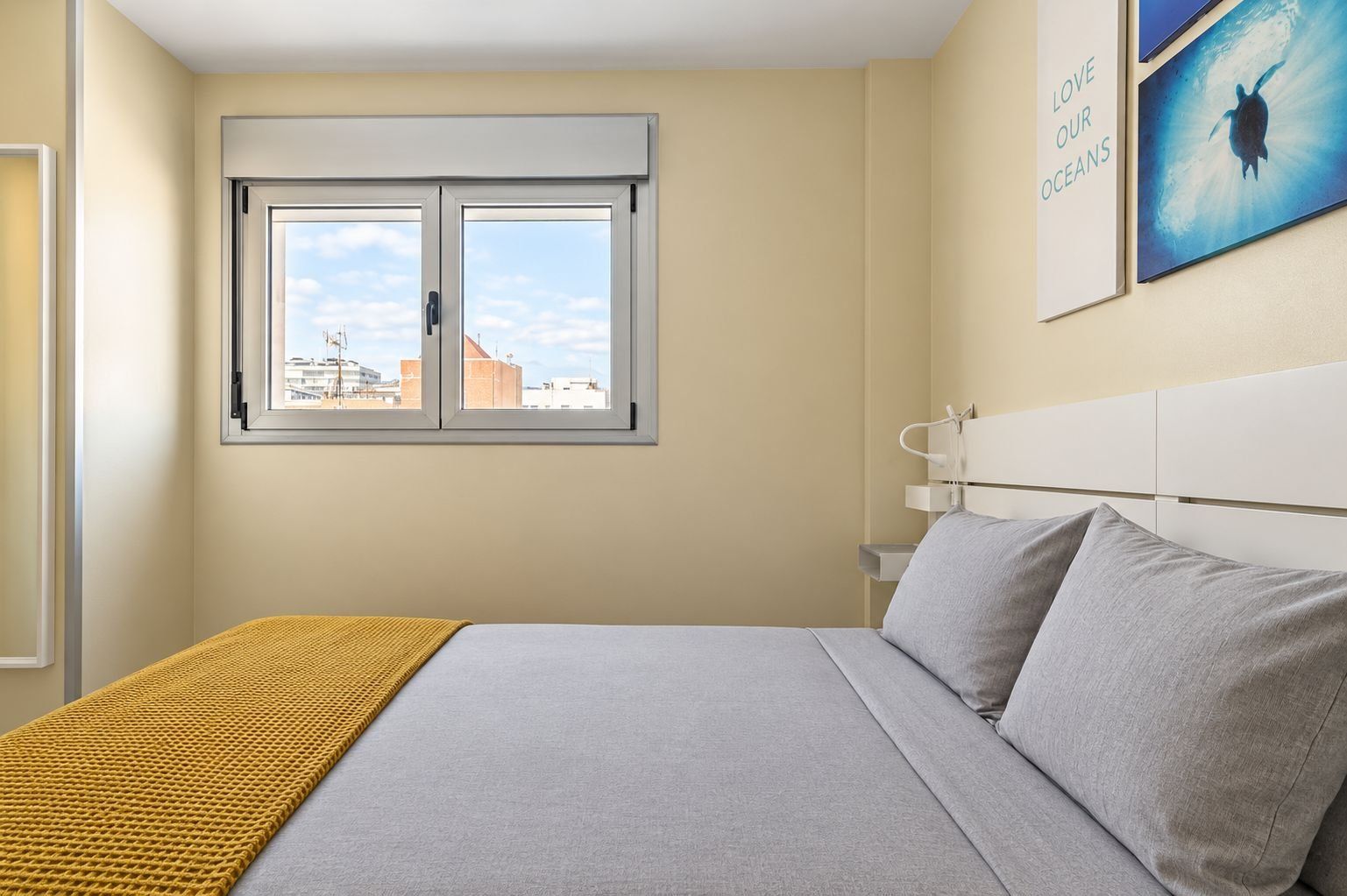 Ein Schlafzimmer mit einem Bett, einem Fenster, einem Wandbild und einem Nachttisch.