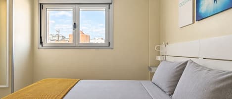A bedroom with a bed, a window, a wall-mounted artwork, and a bedside table.