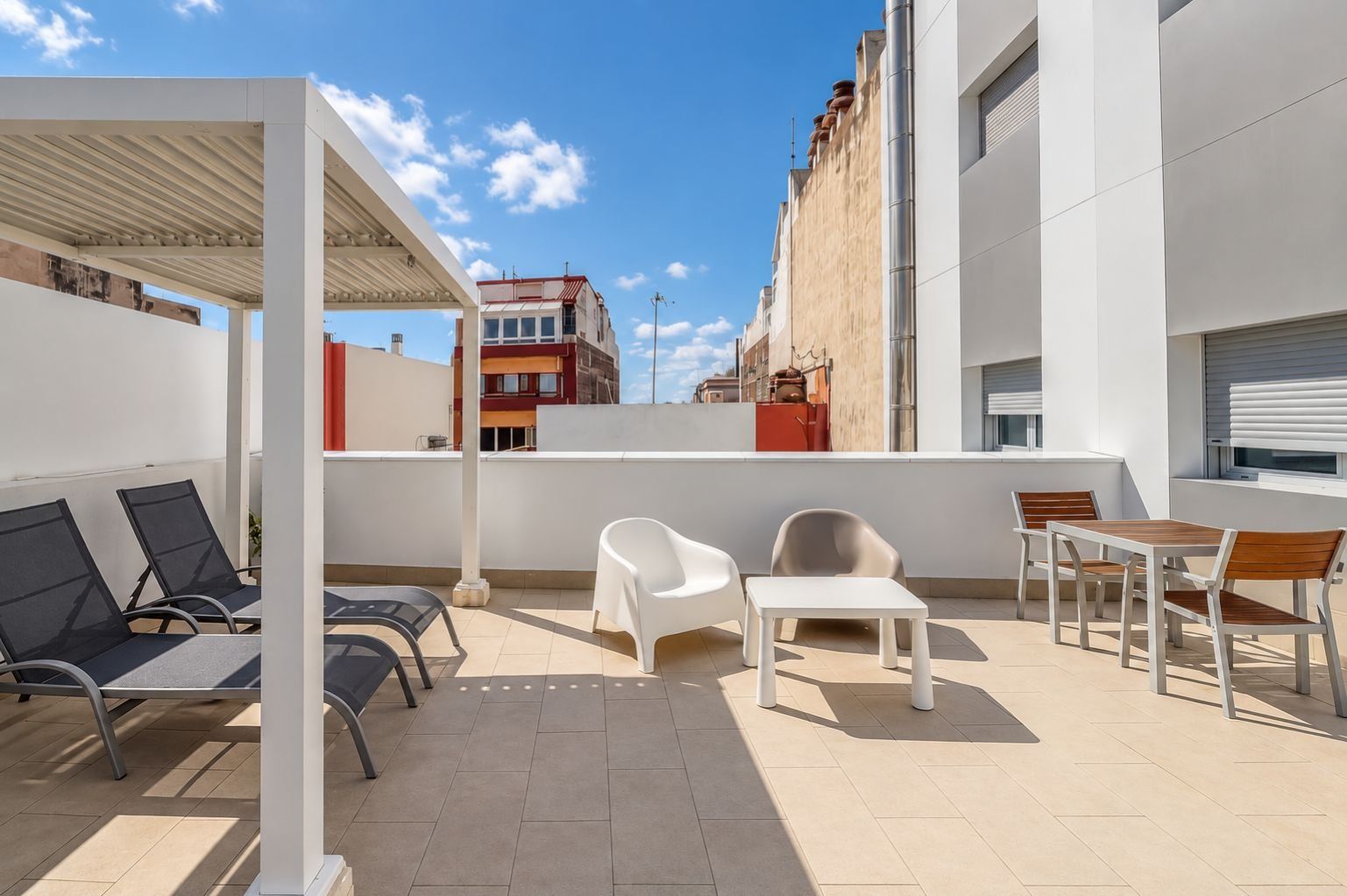 A rooftop terrace with outdoor seating, including chairs and tables, and a view of surrounding buildings.