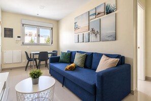 Ein modernes Wohnzimmer mit einem blauen Sofa, einem Esstisch mit Stühlen und einer Zimmerpflanze.