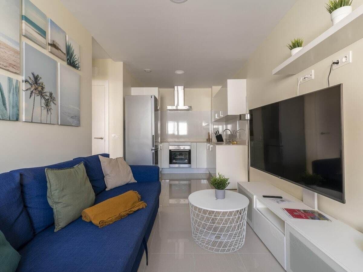 A modern living room with a blue sofa, a flat-screen TV, and a small round table.