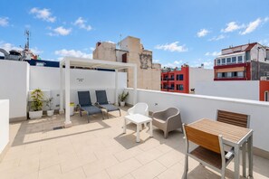 Terraço no telhado com espreguiçadeiras, mesa e plantas em vasos.