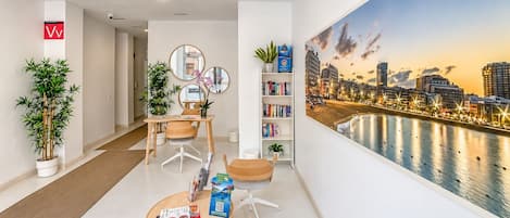 Una camera d'albergo moderna con vista sulla città, un'area pranzo con tavolo e sedie, e una libreria con libri.