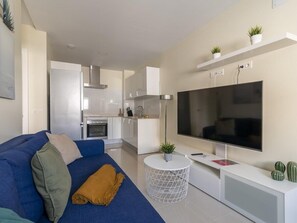 A modern living room with a blue sofa, a flat-screen TV, and a kitchen in the background. - GuestReady - 04A Livian Suites Int 3 Pax/Terraza (Las Palmas de Gran Canaria)