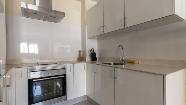 Una cocina moderna con armarios blancos, horno de acero inoxidable y pileta integrada.