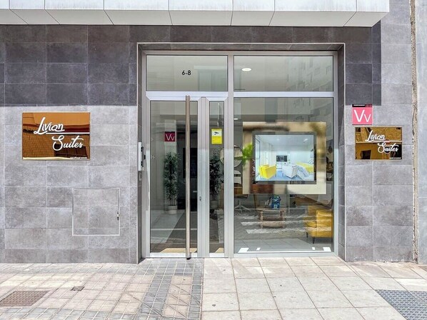 Entrada de hotel com portas de vidro, um letreiro com 'Lyvian Suites' e o logotipo 'W' na parede.