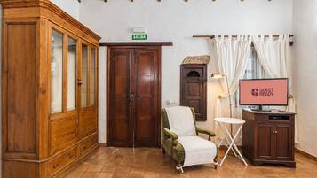 A room with a wooden cabinet, a green armchair, a television displaying 'GUEST READY', and a sign indicating 'SALIDA'.