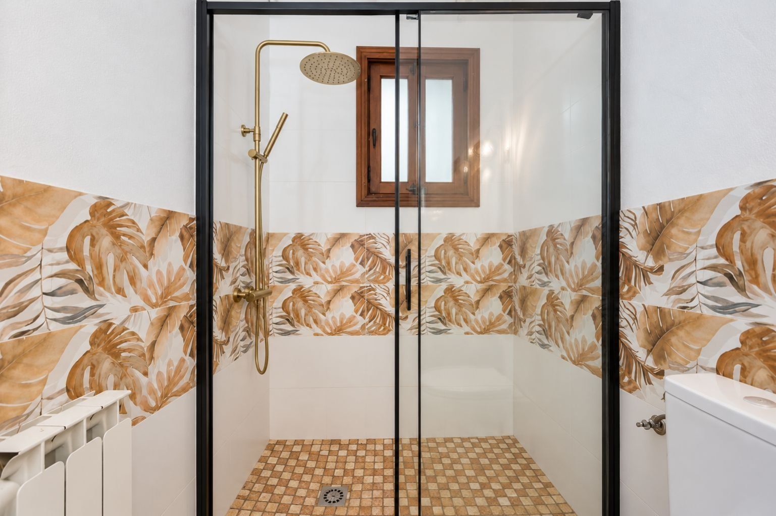 A glass-enclosed shower with a handheld showerhead and a wall-mounted faucet.