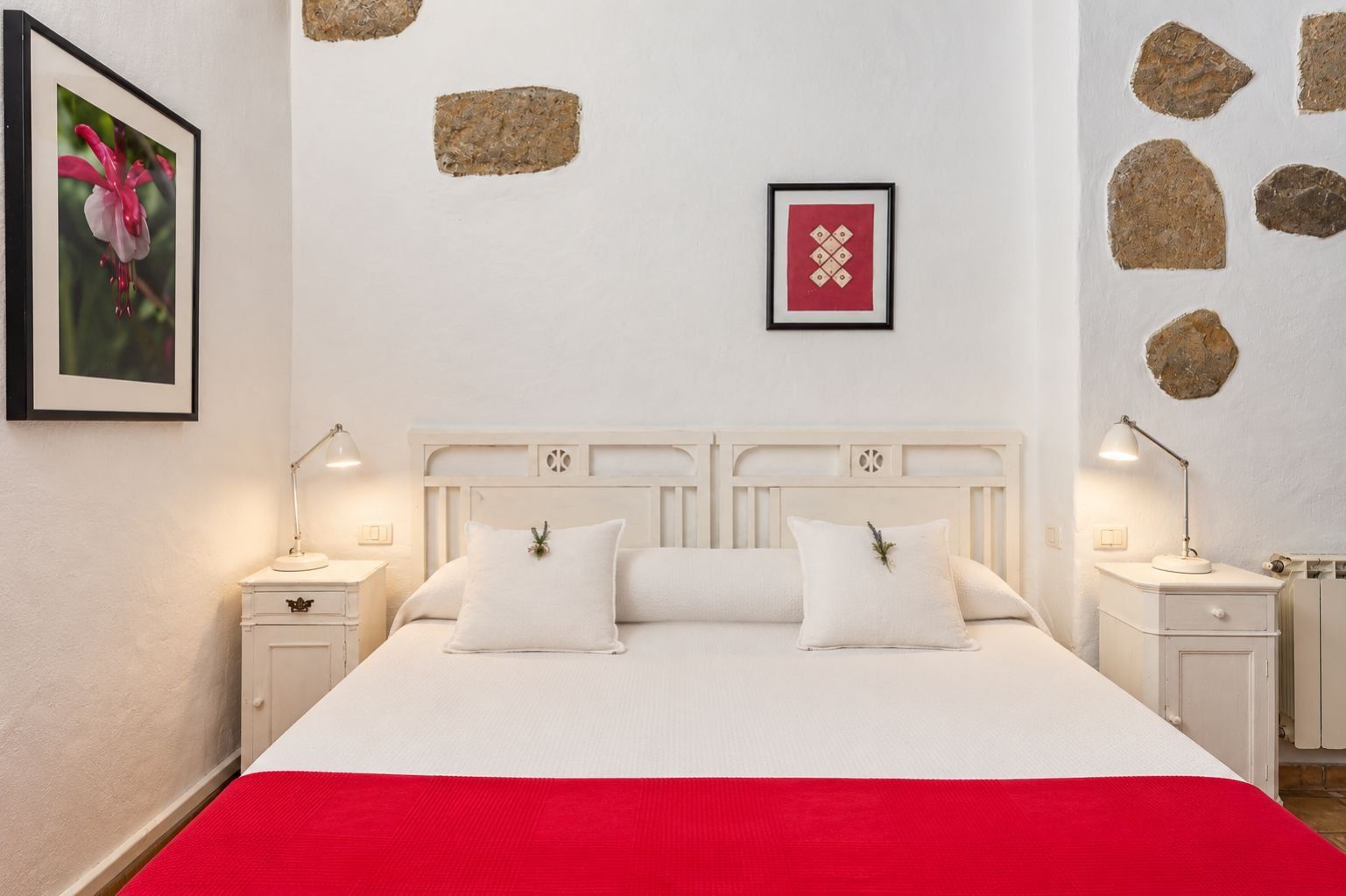 A bed with white bedding, two bedside lamps, and a red throw blanket.