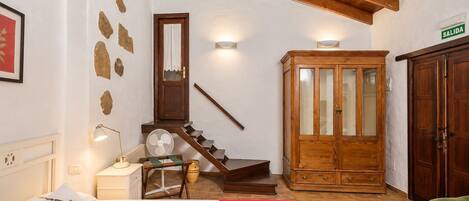 Una habitación de hotel con una cama, un armario de madera, una escalera y una puerta con la inscripción 'SALIDA'.