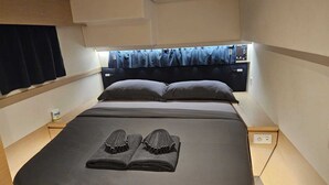 A compact hotel room with a single bed, a window with curtains, a bedside table, and a power outlet.