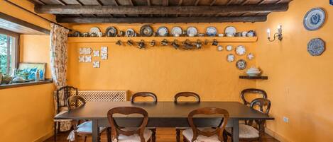 Un comedor con una mesa y sillas de madera, una pared amarilla y una variedad de platos y tazas exhibidos en estantes.