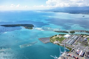 An aerial view of a coastal area with a marina, industrial buildings, and a large cargo ship docked at a port.