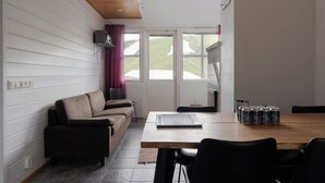 A room with a wooden ceiling, a sofa, a dining table with chairs, and a window with curtains. - Alpine Kajo B5 by Aavalevi (Levi)