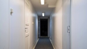 A narrow hallway with white walls, a carpeted floor, and a door at the end leading to a dark room. - Alpine Kajo B5 by Aavalevi (Levi)