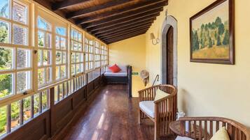 A room with a wooden ceiling, large windows, a bed, a chair, and a painting on the wall.