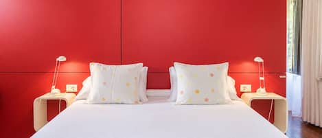 A bed with white bedding and two pillows with polka dots, flanked by bedside tables with lamps, in a room with red walls.
