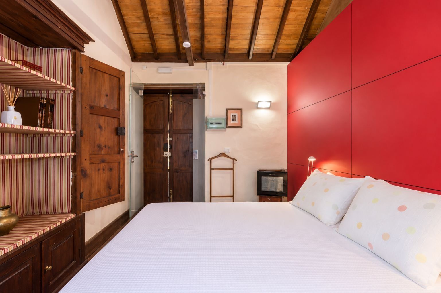 Une chambre avec un grand lit, une armoire en bois et un mur d’accent de couleur rouge.