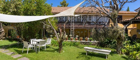 Un patio con una mesa y sillas blancas, un banco y una variedad de plantas en macetas.