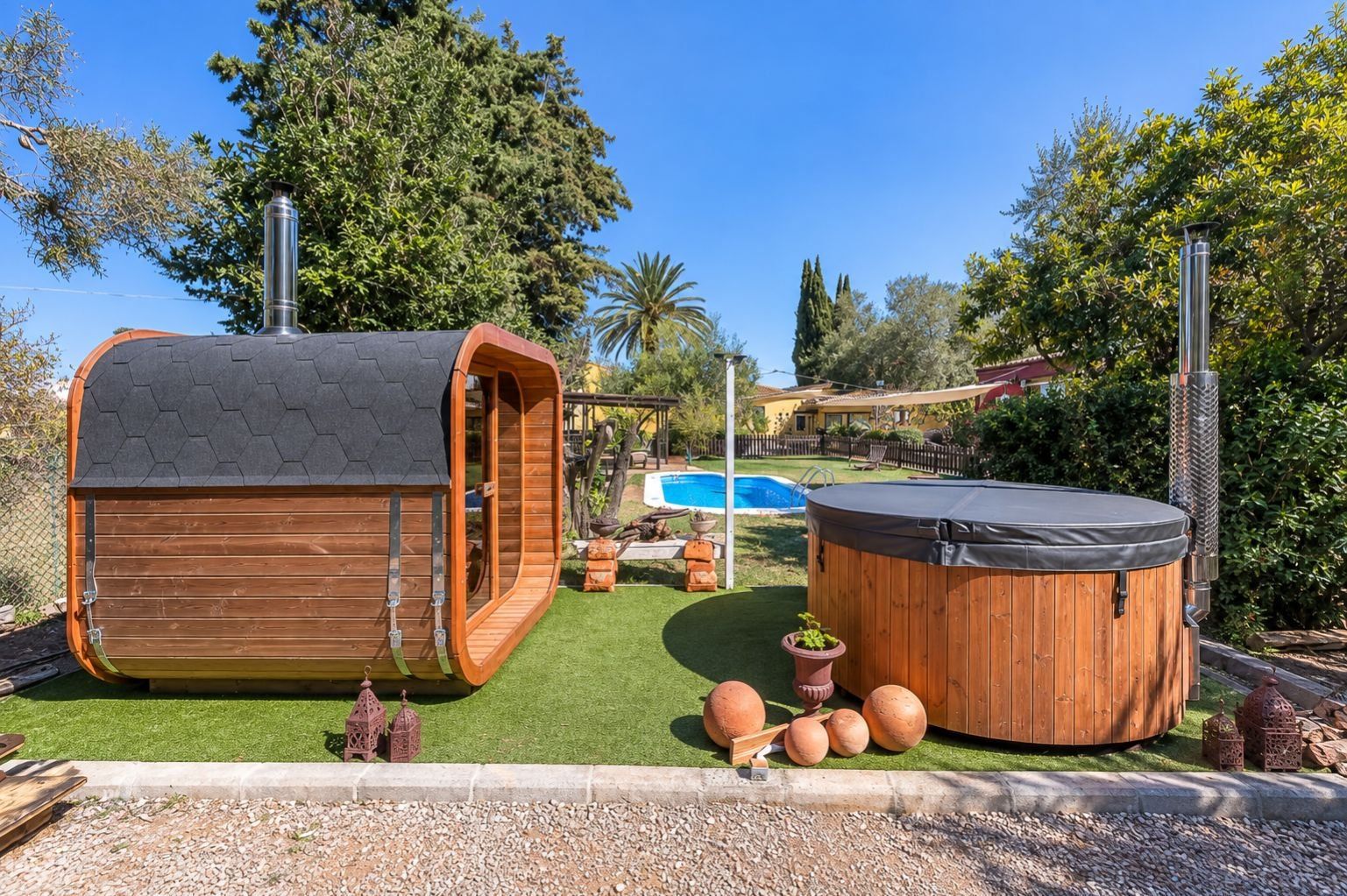 Ein hölzerner Whirlpool und ein Holzbau mit sechseckigem Dach in einem Garten mit Schwimmbad.