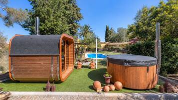 Ein hölzerner Whirlpool und ein Holzbau mit sechseckigem Dach in einem Garten mit Schwimmbad.