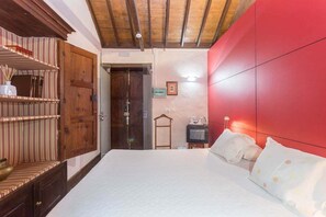 Een slaapkamer met een houten garderobe, een bed met wit bedlinnen, een rode accentmuur en een klein nachtkastje met een lamp.