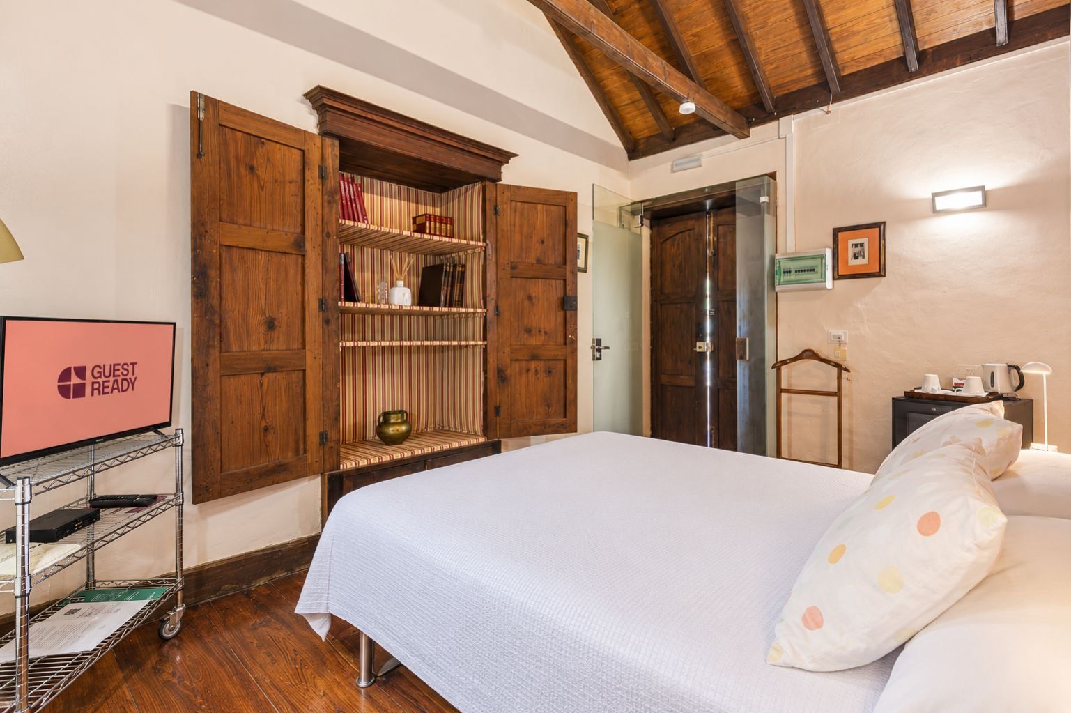 Habitación de hotel con una cama, un armario de madera, un televisor y un escritorio con lámpara.