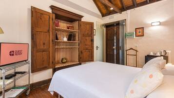 Habitación de hotel con una cama, un armario de madera, un televisor y un escritorio con lámpara.