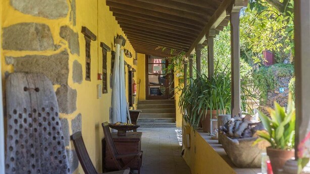 A covered corridor with stone walls, wooden furniture, and potted plants. - GuestReady - Las Calas 9 Double Room Rosa (Las Palmas de Gran Canaria)