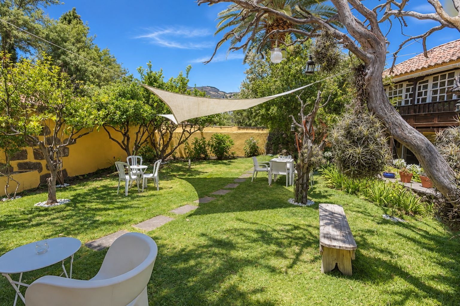 Un jardín bien cuidado con un patio, mobiliario exterior y diversas plantas.