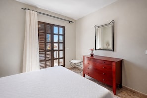 A bedroom with a bed, a dresser, a mirror, and a window with curtains.