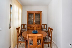 A dining room with a round wooden table, six chairs, a cabinet with glass doors, and a window with curtains. - GuestReady - Duplex Turman Agaete Terrace (Agaete)