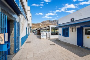 A narrow street with buildings on both sides, a sign for a restaurant, and a mountain in the background. - GuestReady - Duplex Turman Agaete Terrace (Agaete)