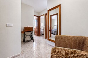 Um corredor com um banco de madeira, uma máquina de costura e um espelho refletindo um quarto.