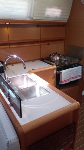 A compact kitchenette with a stainless steel sink, a kettle, and a stove. - Sibenik Sun and Beach Sailing Extravaganza (Skradin)