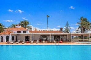 Ein Hotel mit Schwimmbad, Liegestühlen und Palmen.