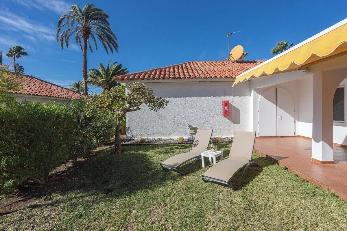 A house with a red-tiled roof, a white exterior wall, and a small patio area with two sun loungers and a white table.
