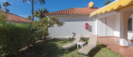 A house with a red-tiled roof, a white exterior wall, and a small patio area with two sun loungers and a white table.
