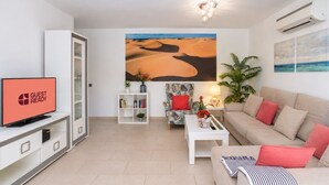 Uma sala de estar moderna com uma TV de tela plana, uma estante, um sofá, uma mesa de centro e um quadro com uma paisagem desértica.