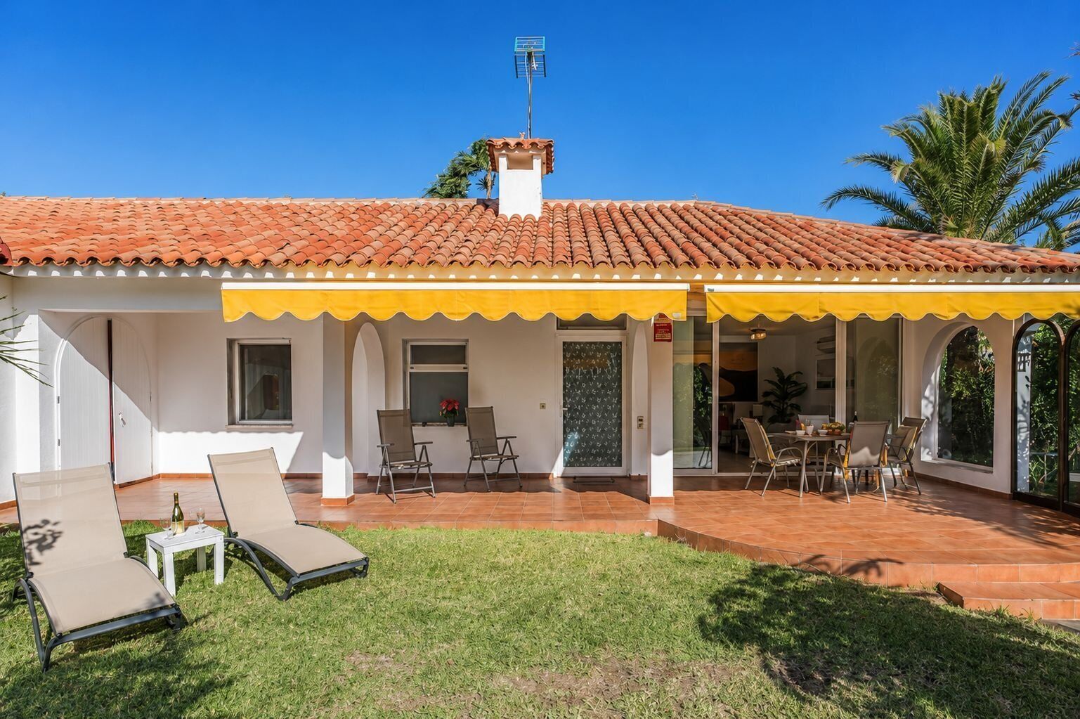 A house with a tiled roof, a covered patio with chairs, and a lawn.