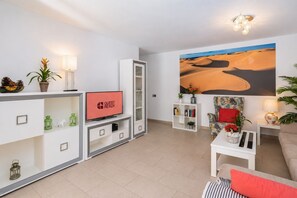 Un salon moderne avec un téléviseur à écran plat, une bibliothèque, un canapé et un grand tableau représentant un paysage désertique accroché au mur.