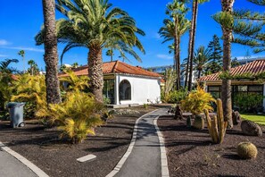 A pathway leading to a building with a red-tiled roof, surrounded by palm trees and cacti. - GuestReady - Sun Club Terrace and Pool (San Bartolomé de Tirajana)