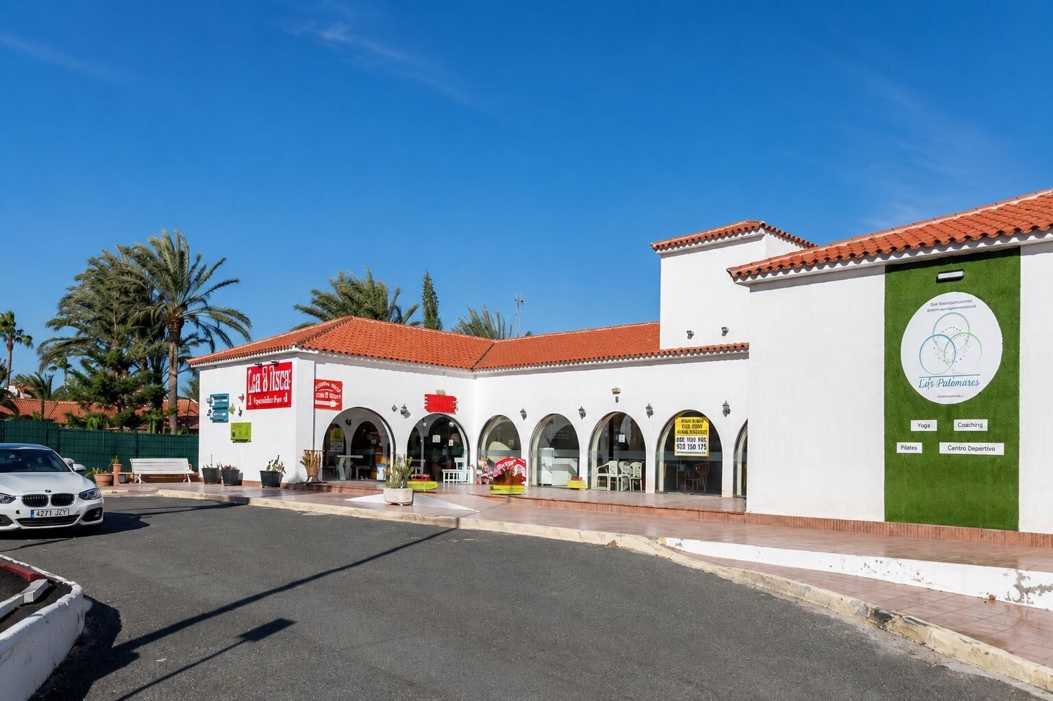 A building with a white facade and red roof tiles, featuring multiple arched doorways and a green banner with logos.