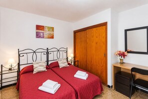 A double bed with red bedding, a wooden wardrobe, a desk with a chair, and a mirror on the wall. - GuestReady - Bello Horizonte Sea View and Pool (San Bartolomé de Tirajana)