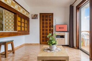 A room with a wooden door, a television displaying 'GUEST READY', a potted plant on a table, and a view of the outside through a glass door. - GuestReady - Bello Horizonte Sea View and Pool (San Bartolomé de Tirajana)