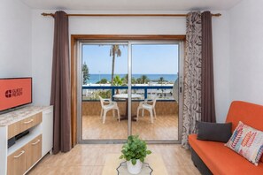 A room with a sliding glass door leading to a balcony with a view of the sea, a television on a cabinet, and a sofa with decorative pillows. - GuestReady - Bello Horizonte Sea View and Pool (San Bartolomé de Tirajana)